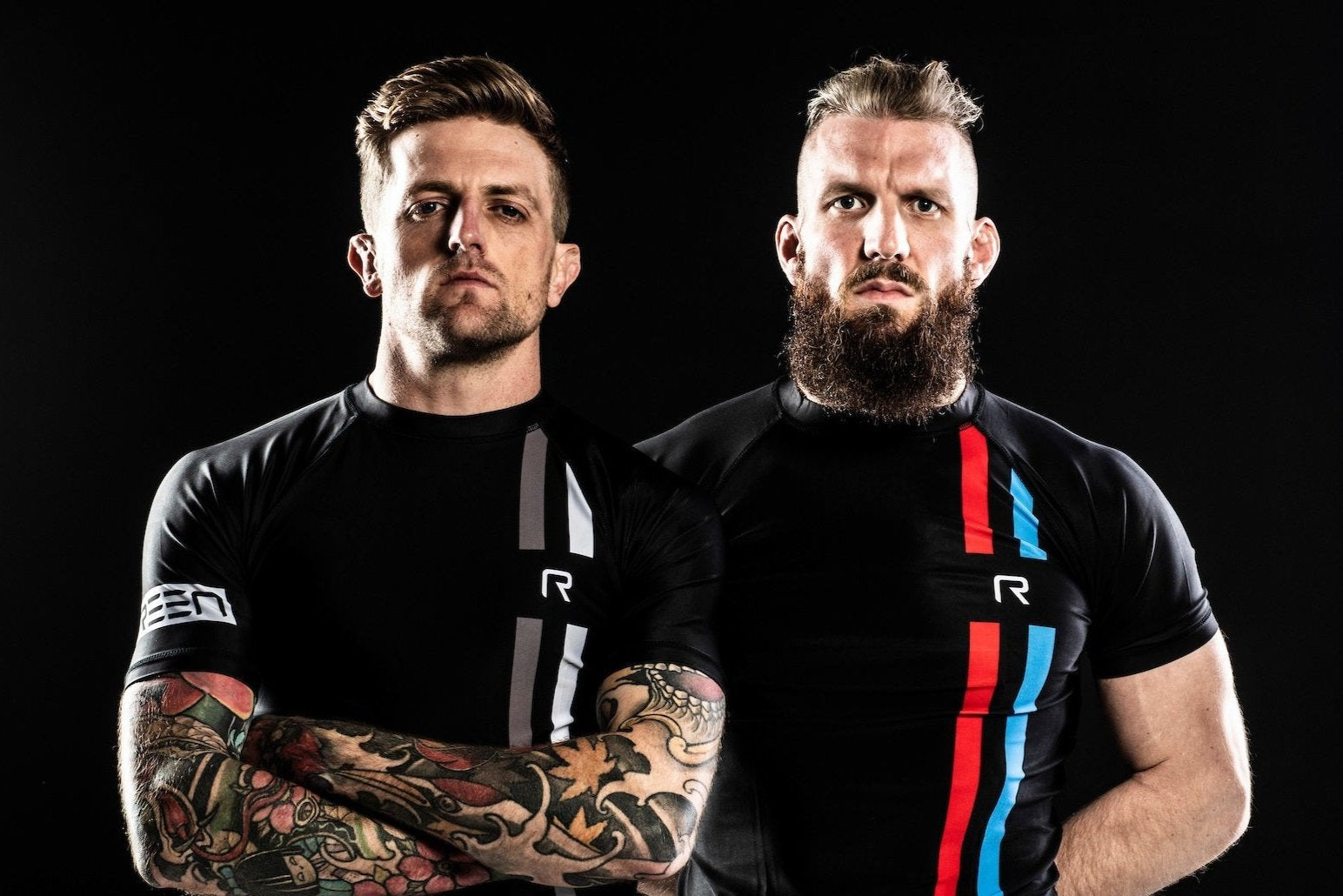 Two men wearing black athletic shirts with visible branding against a dark background